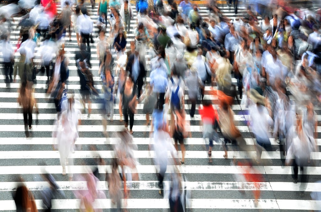 Blurred photo of a crowd of people walking over a road on a zebra crossing.